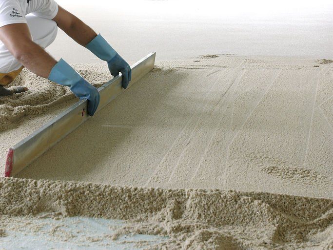 Eine Person glättet sandfarbenen Beton mit einem Werkzeug, trägt blaue Handschuhe.