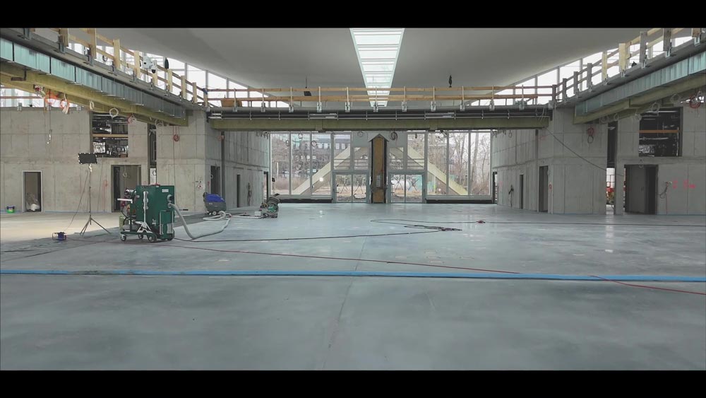 Großer, leerer, grauer Raum mit Oberlicht, Rohbau. Baustellenmaterialien und Geräte auf dem Boden.