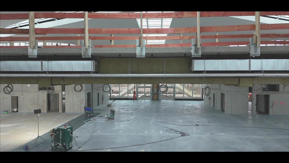 Große, leere Halle mit Betonwänden, Lichtdurchflutung durch Oberlichter und sichtbarer Kabel.