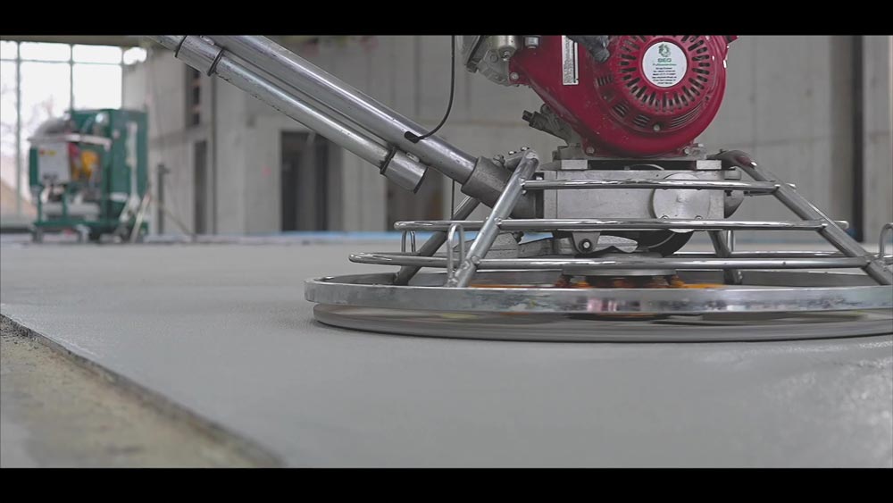Eine Betonglättmaschine glättet eine graue Betonoberfläche in einer unfertigen Halle.