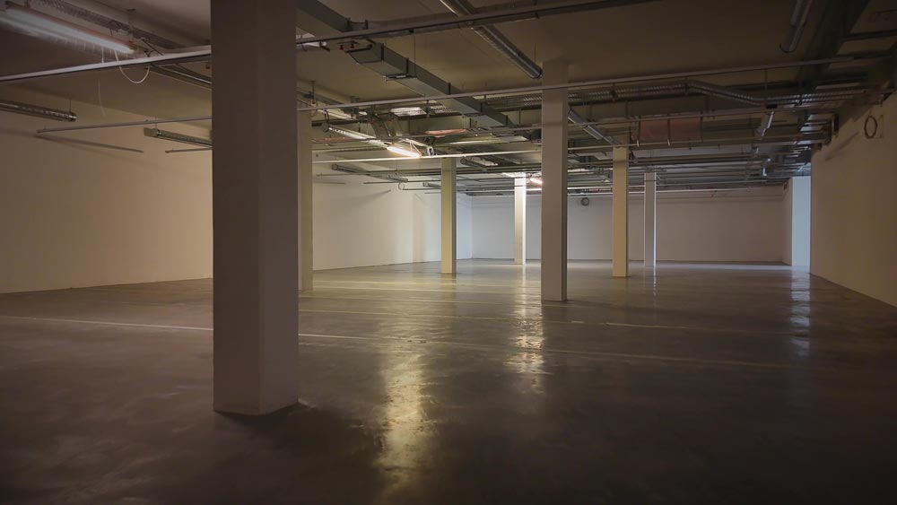 Leerer, beleuchteter Kellerraum mit Betonboden und mehreren Säulen.