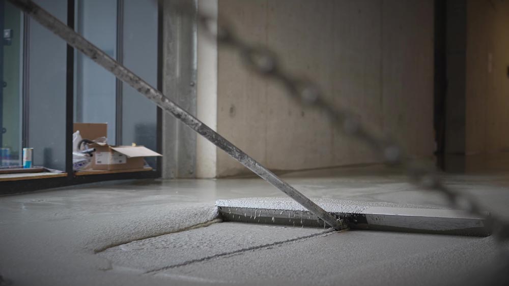 Frisch gegossener Betonboden in modernem Raum mit Karton und Werkzeugen am Rand.