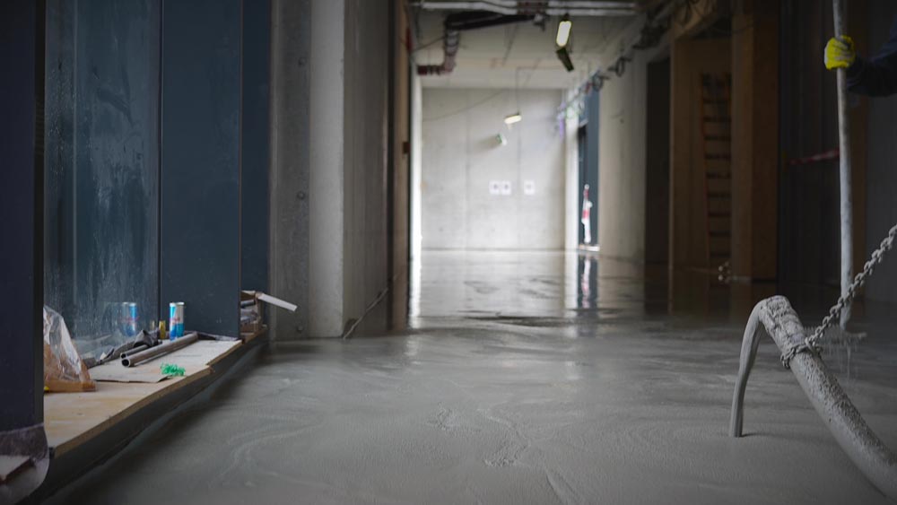 Flur eines Bauprojekts mit gepumpter grauer Betonmasse und Baustellenmaterialien.