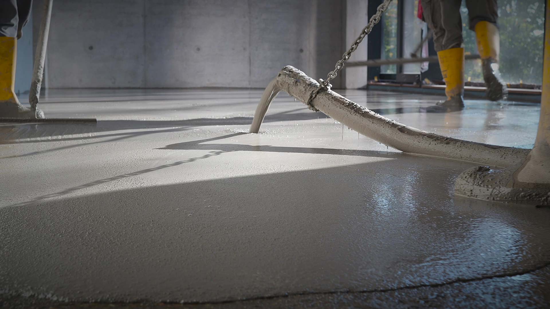 Betonboden wird gegossen; Arbeiter in gelben Gummistiefeln; glatte, graue Oberfläche.